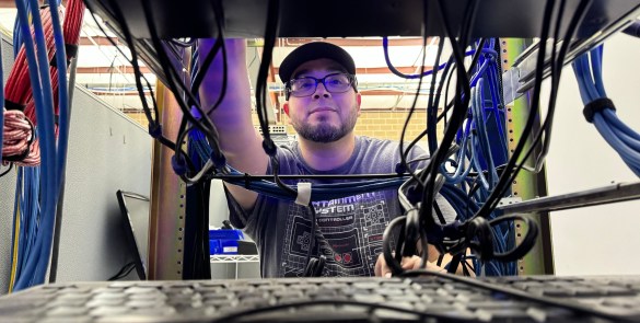 Image illustrating careers NDI, a collaborator is standing behing a server rack.