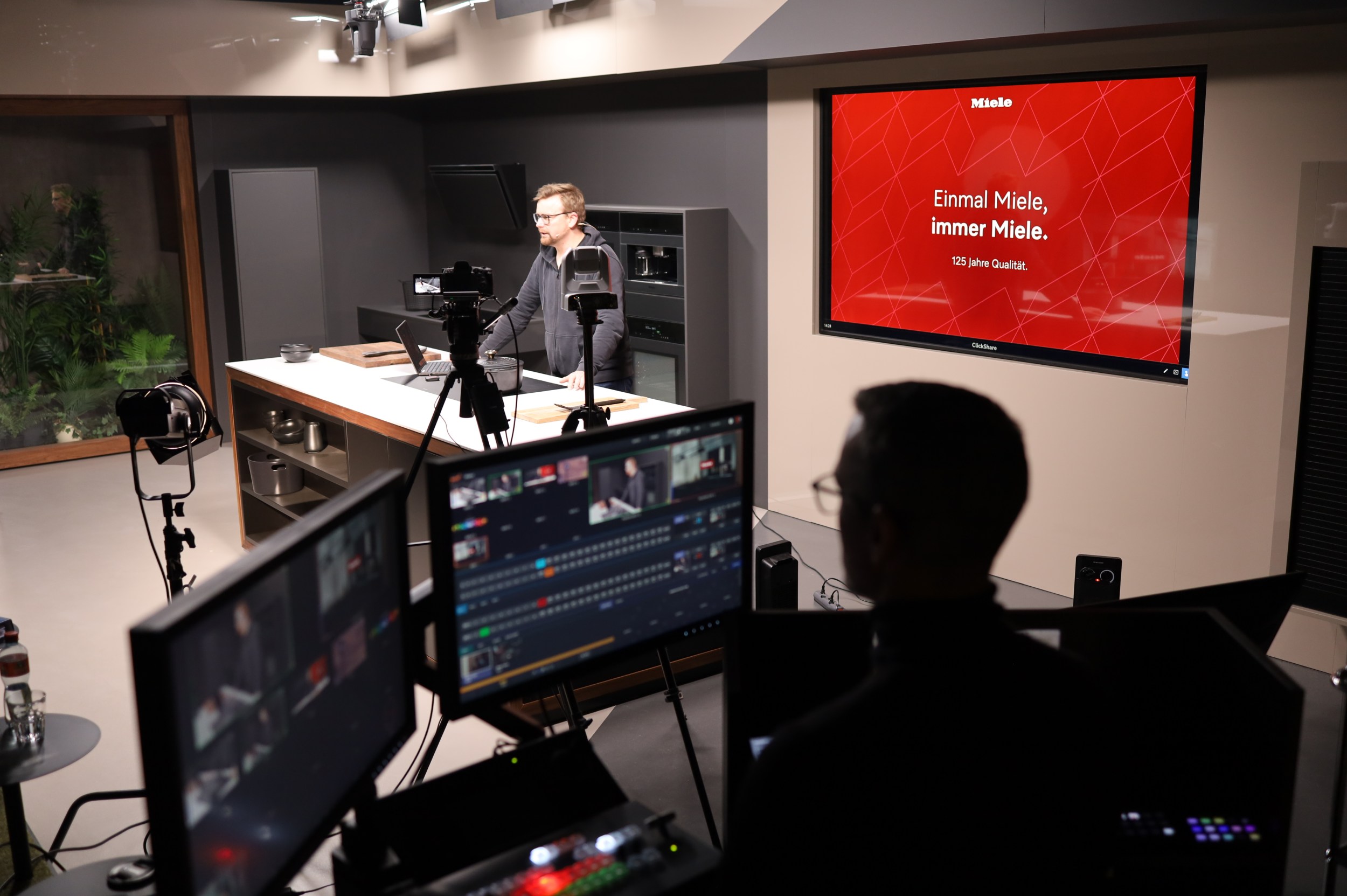 A presenter takes his position behind the Miele-branded kitchen island, surrounded by Canon cameras
